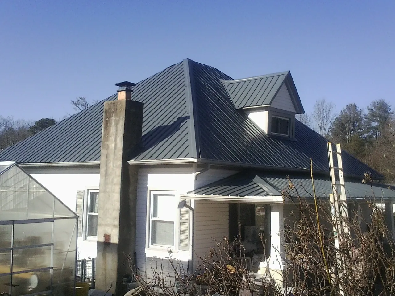 Dark blue standing seam metal roof on a white farmhouse with dormer — Slate & Tile Roof Repair by Roofing Brothers in Plato