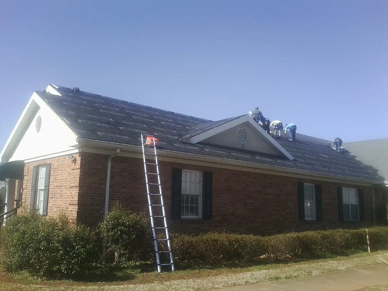 Crew tearing shingles off a brick ranch roof with a ladder set — Emergency Roof Repair work by our crew in Plato