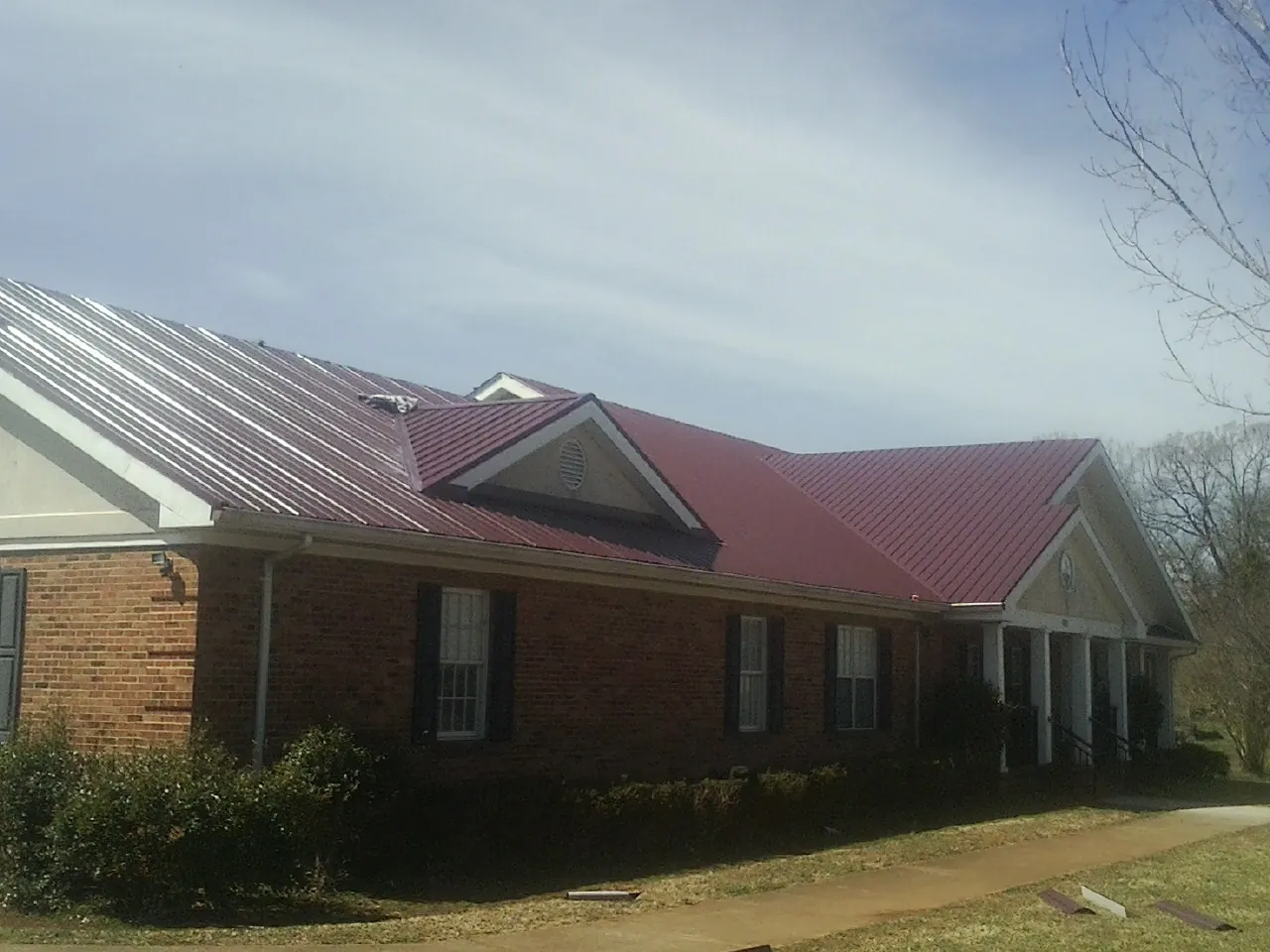Red metal roof with gabled entries on a long brick building, from a Hail Damage Roof Repair job in Plato