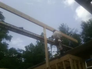 Carpenter setting a ridge beam over a new addition frame in Plato