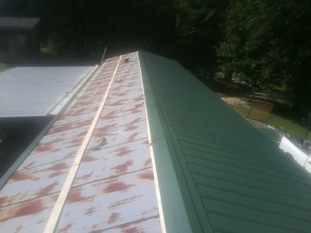 Old rusted panels beside newly installed green metal roofing — Wind Damage Roof Repair by Roofing Brothers in Plato