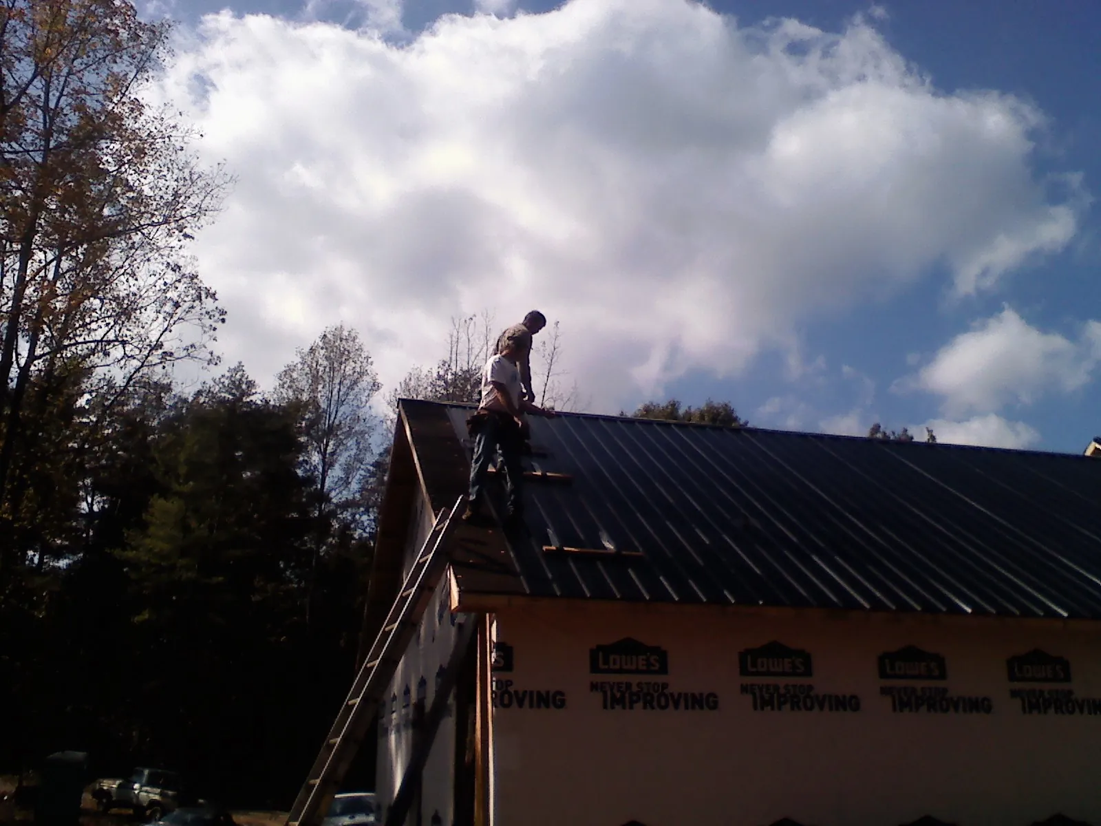 Roofer fastening dark metal panels high against a cloudy sky, from a Roof Inspection job in Plato