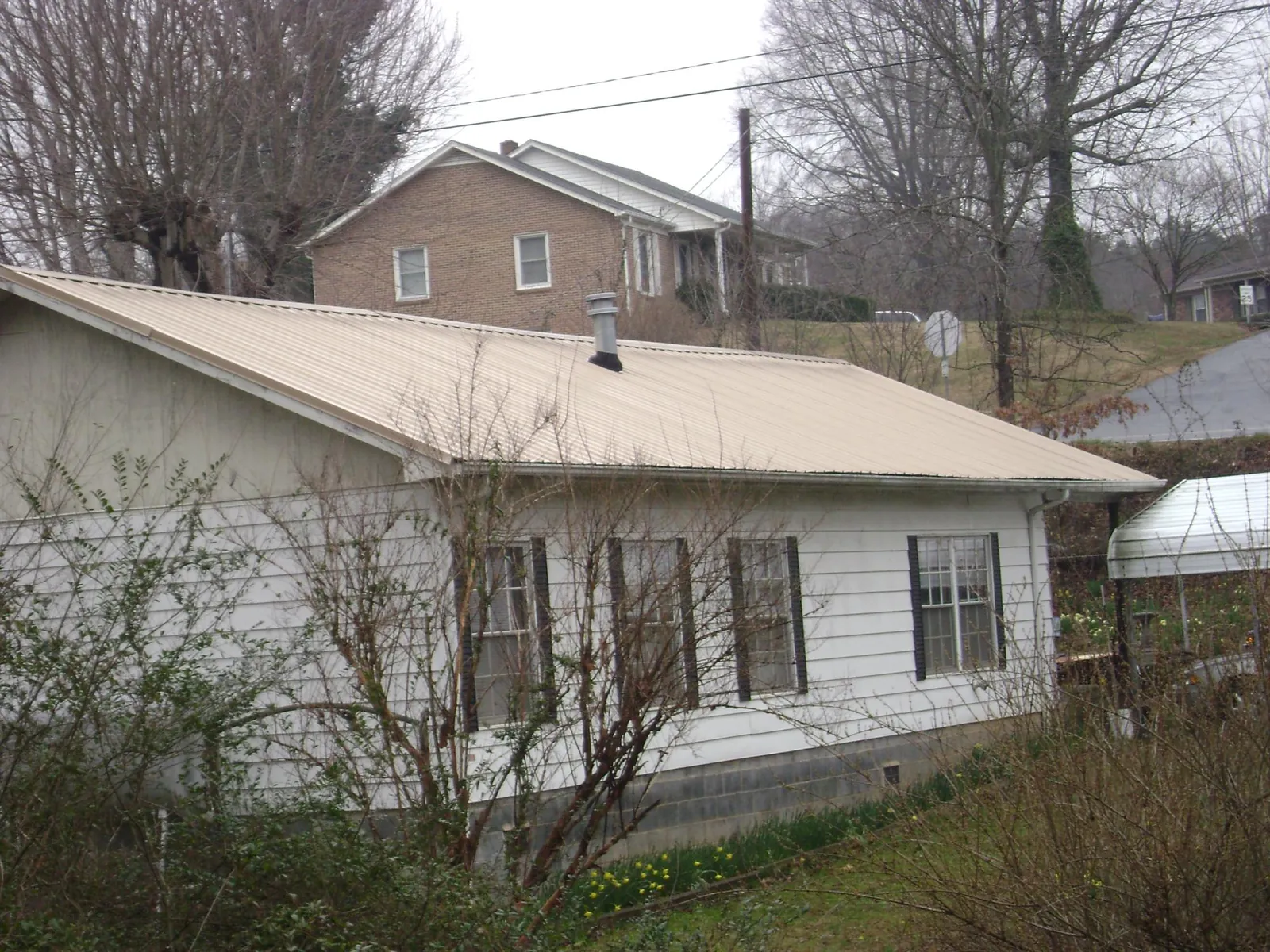 Tan metal roof on a white sided house set into a hillside — Commercial Roofing by Roofing Brothers in Plato