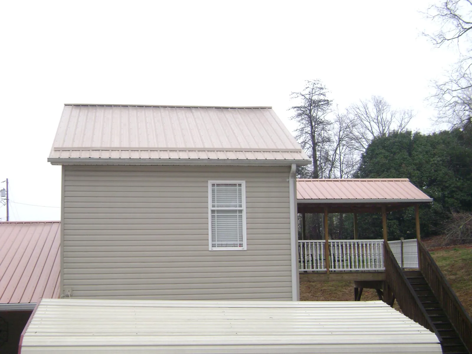 Tan metal roofs on a two story addition and attached porch, from a Roof Replacement job in Plato